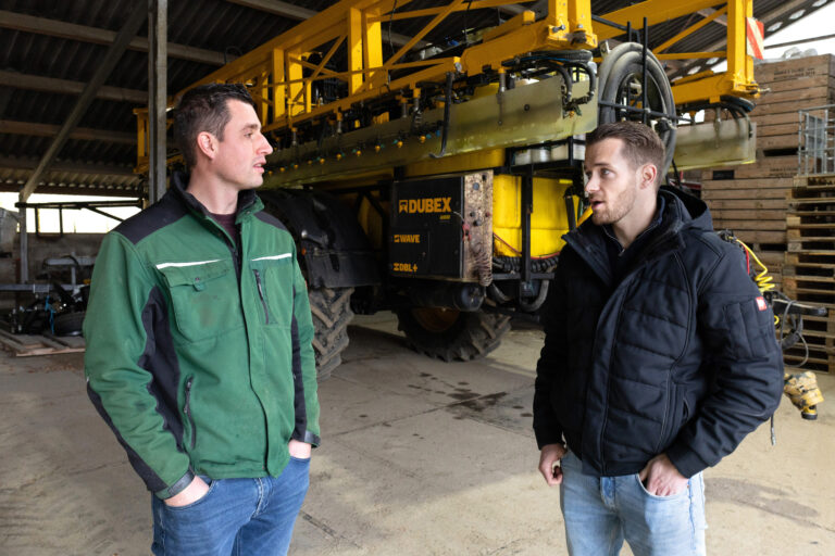 Mannen in gesprek met op de achtergrond de spuit